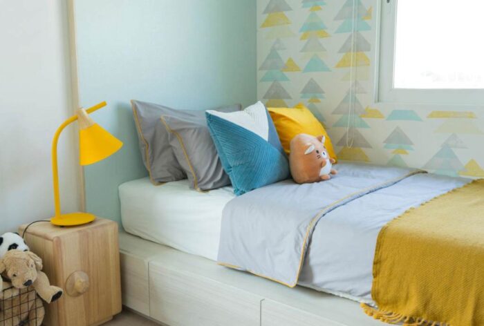 Many dolls setting on bed with pillows in kid bedroom